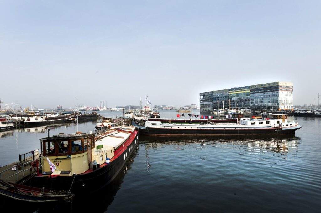 Havenzicht met woonboten aan de Van Diemenstraat en een modern gebouw op de achtergrond in Amsterdam.